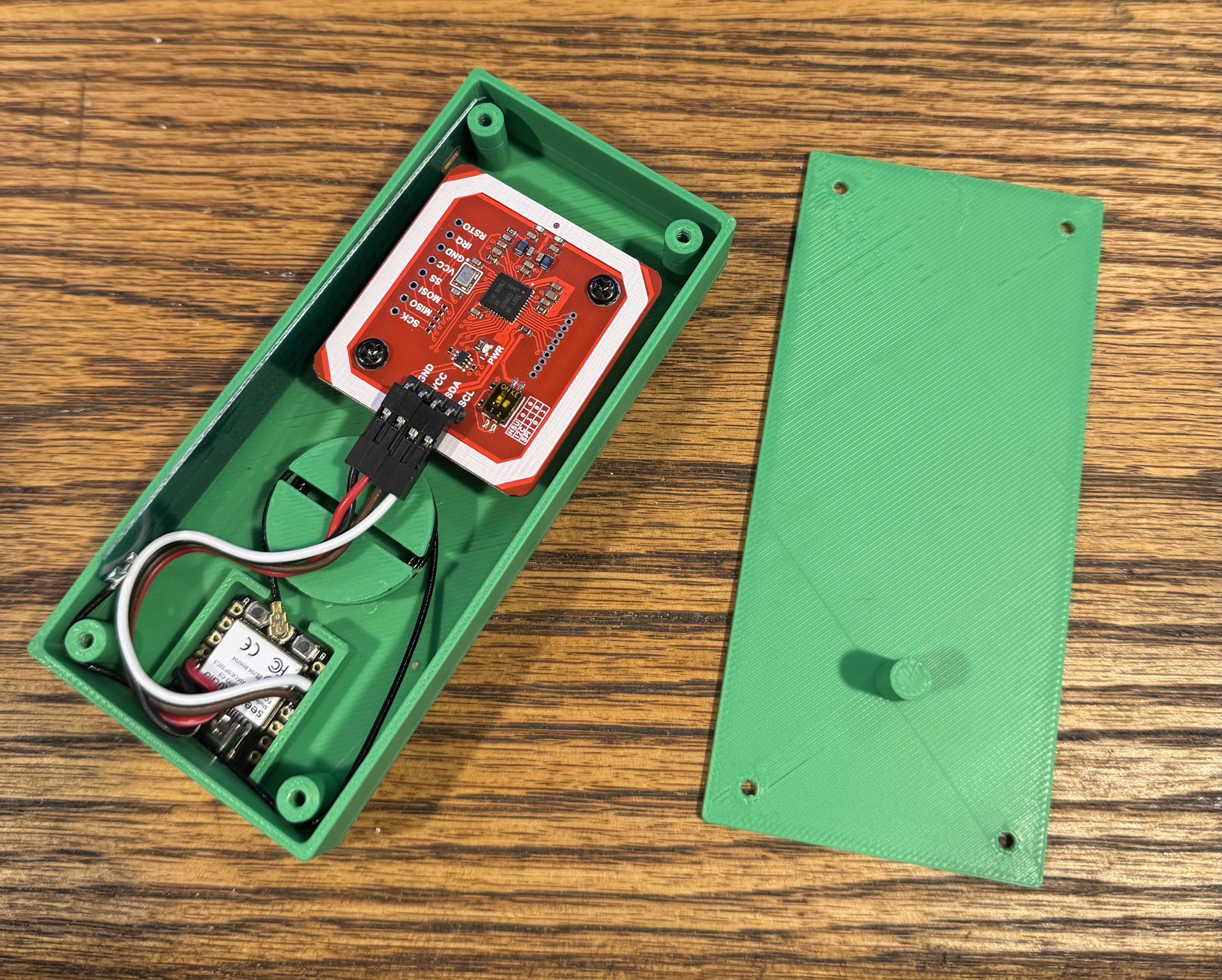 Open green 3D-printed enclosure with the PN532 board mounted up top, the XIAO ESP32-C3 wired below, and the antenna cable wound around a built-in spool
